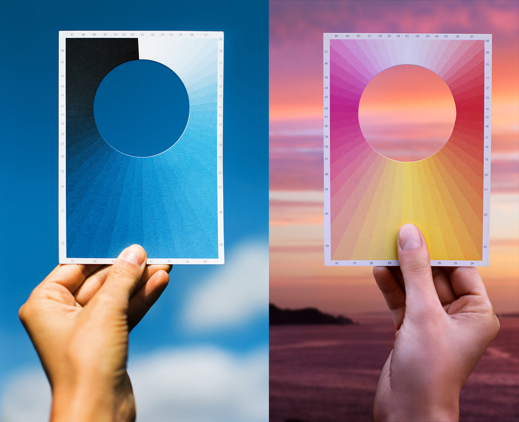 A hand holding a postcard up to the sky, which you can see through a round hole in the upper center portion of the card. Around the card, radiating from where the center would be are dozens of shades of blue, allowing you to identify the exact shade of blue in the sky today. There is a second photo, identical, except with a shades of pink/yellow/red for morning or evening skies.